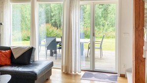 Un salon avec un canapé en cuir noir, une petite table et une vue sur une terrasse extérieure agrémentée de chaises et de plantes.