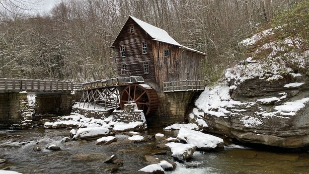 A wooden watermill with a wooden bridge and a stone structure.