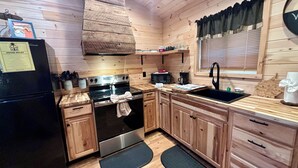 A compact kitchen with wooden cabinets, a black refrigerator, a stove, and a microwave.