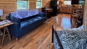 A cozy cabin interior with a wooden ceiling, a ceiling fan, a sofa, a dining table, and a kitchen area.