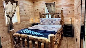 A wooden cabin bedroom with a rustic bed frame, a quilted bedspread, and a window with a star-patterned curtain.
