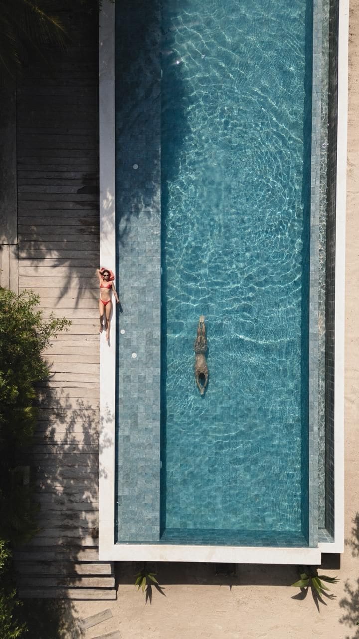 A rectangular swimming pool with clear water, surrounded by a wooden deck and a concrete edge.