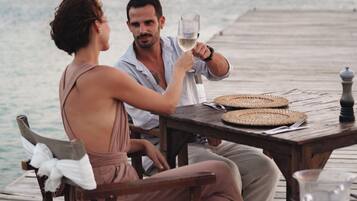 Una pareja cena en una terraza de madera con vista al mar.