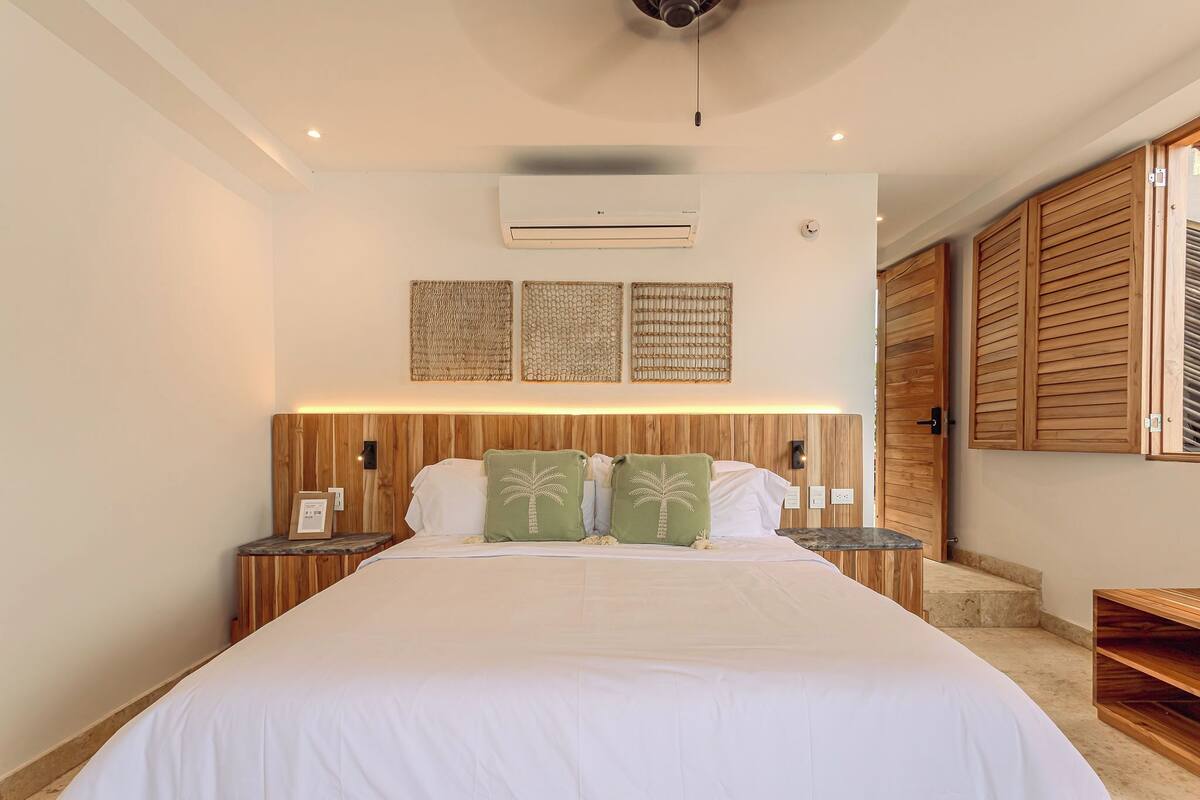 A bedroom with a large bed, wooden headboard, wall-mounted air conditioning, and a wooden wardrobe.