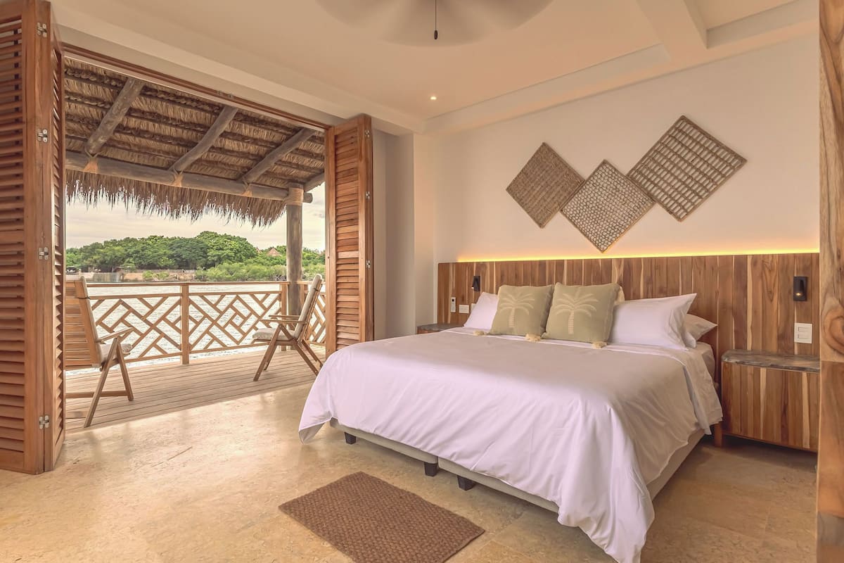 A bedroom with a large bed, wooden headboard, and a view of greenery outside.
