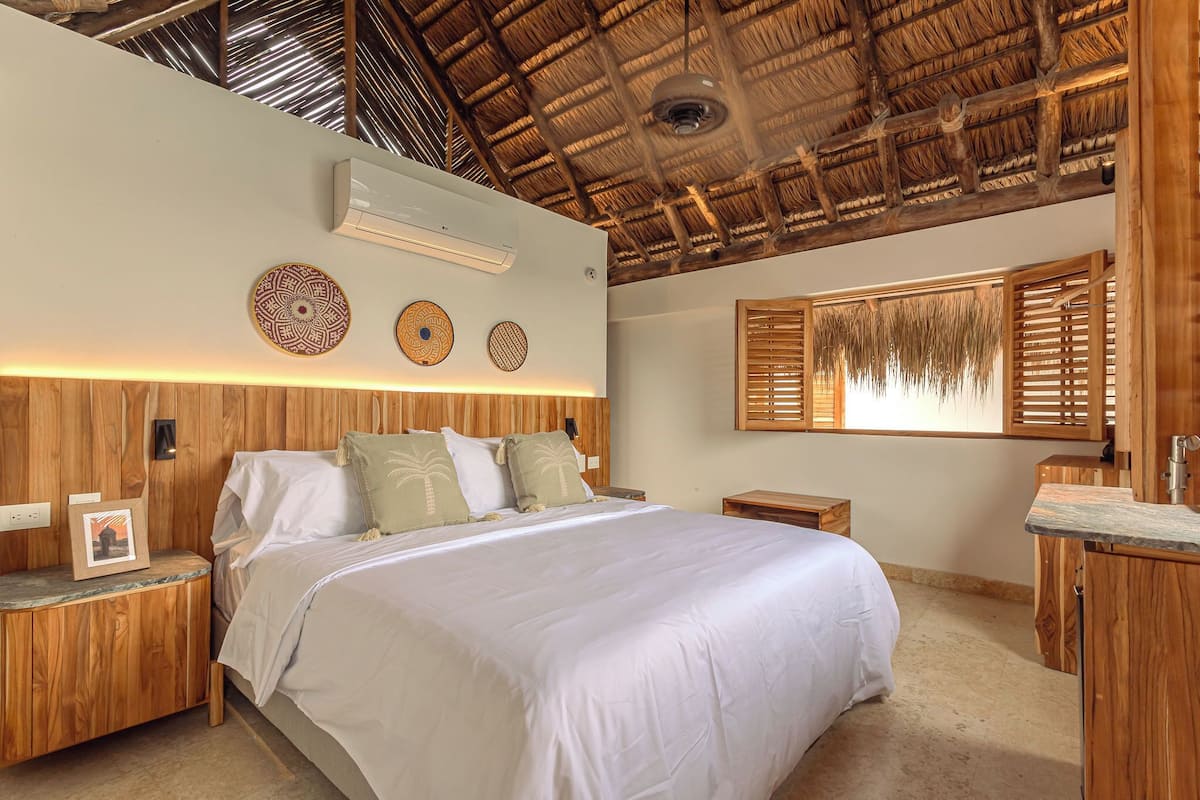 A bedroom with a wooden headboard, a bed with white bedding, a nightstand with a picture frame, and a window with wooden shutters.