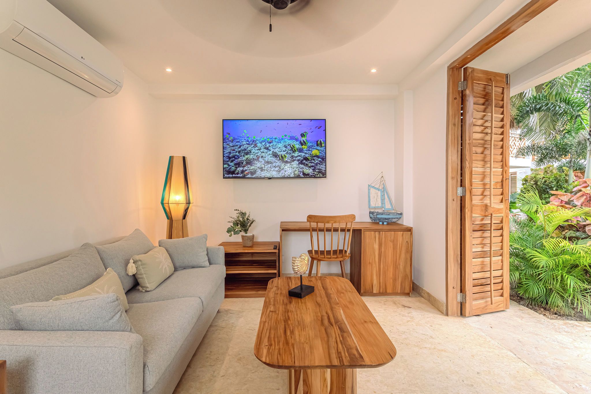 A modern living room with a sofa, coffee table, TV, and a wooden door leading to a garden.