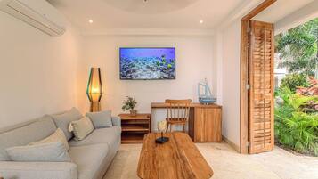 Een moderne woonkamer met een bank, salontafel, televisie en een houten deur naar een tuin.