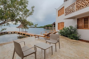 A serene outdoor seating area with a view of the water, wooden deck, and a building with wooden shutters. - Soy Local Islawa (Cartagena)