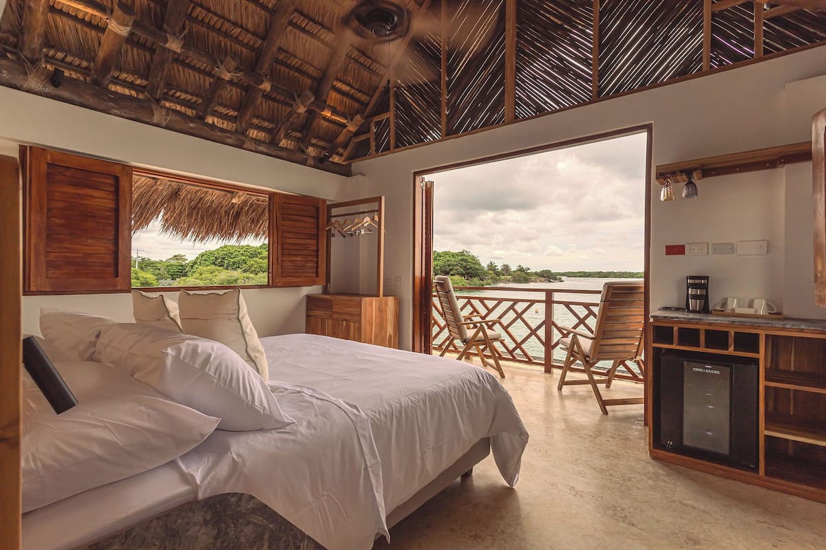 A bedroom with a bed, wooden furniture, a minibar, and a balcony with a view of greenery.