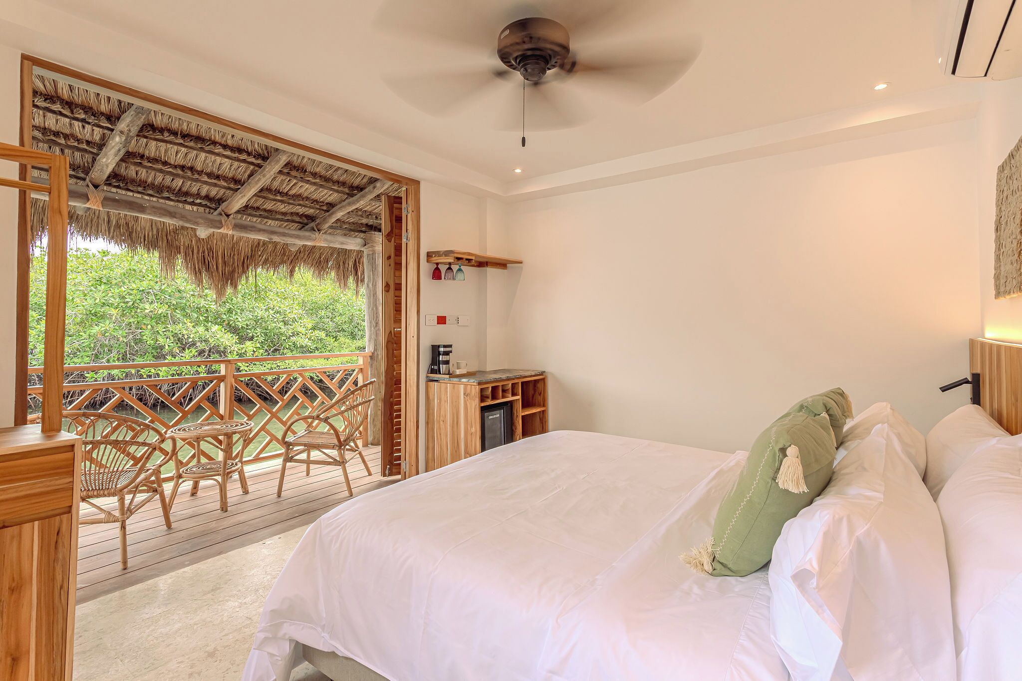 A bedroom with a bed, a small desk, and a view of greenery outside.