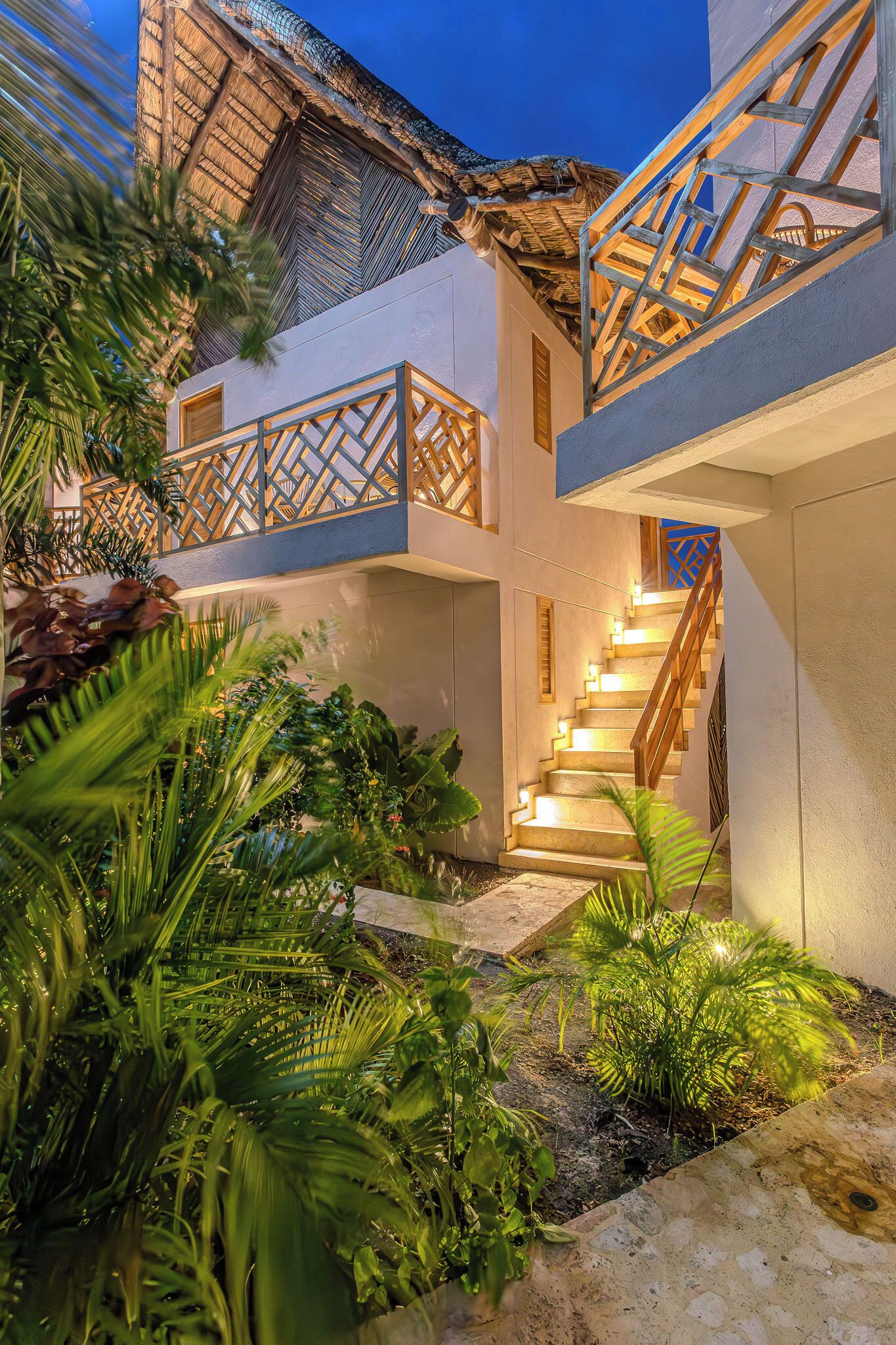 Un edificio moderno con una escalera que conduce a un balcón, rodeado de abundante vegetación.