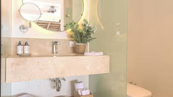 Un baño con un espejo redondo, un lavabo con artículos de aseo, un banco de madera y un inodoro.
