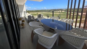 Un balcón con mobiliario de mimbre, una mesa de vidrio y vistas a un campo de golf.