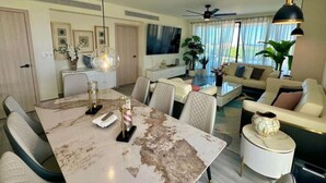 Amplia sala de estar con mesa de comedor, asientos cómodos, televisor y vistas al exterior.