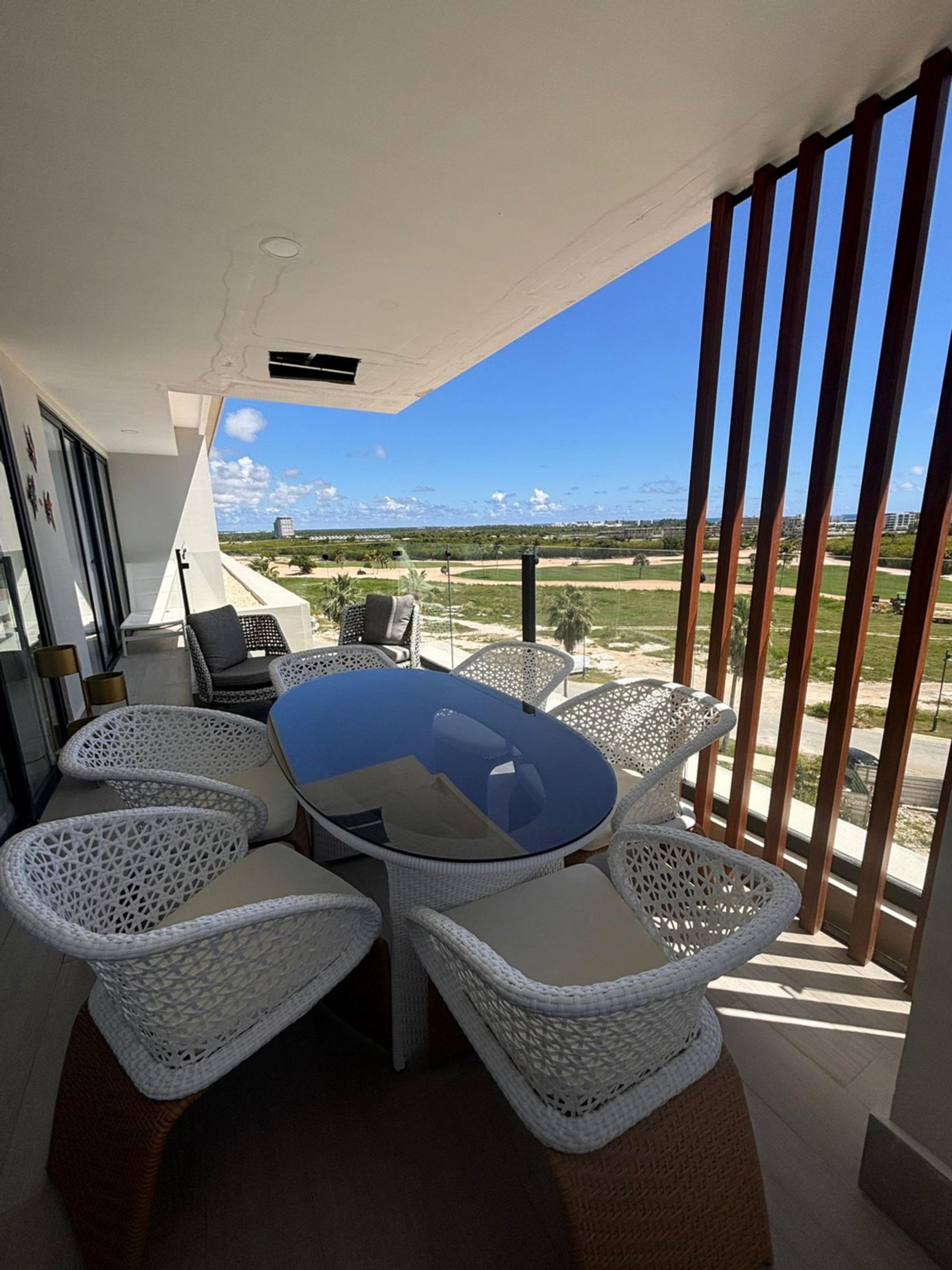 Een moderne eethoek buiten met een glazen tafel en rieten stoelen, met uitzicht op een prachtig landschap.