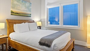 A neatly made bed with white linens and a grey throw blanket, a wooden headboard, and a painting of a landscape on the wall. - Pacific Place: Mountains On Main (Telluride)