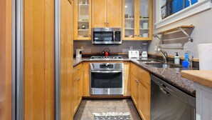 A compact kitchen with wooden cabinets, a stainless steel microwave, an oven, a toaster, and a dishwasher. - Pacific Place: Mountains On Main (Telluride)