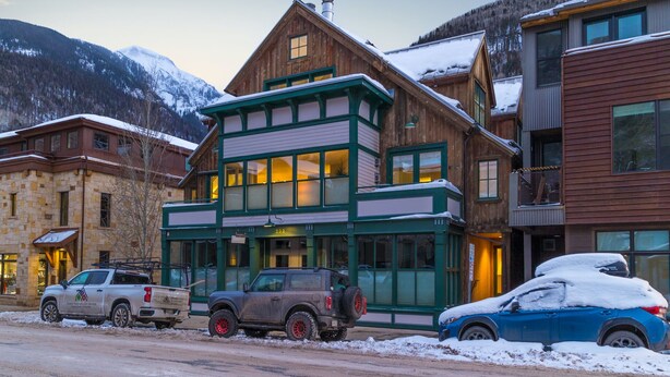 A two-story wooden building with large windows and a balcony, located in a snowy mountainous area. - Pacific Place: Mountains On Main (Telluride)