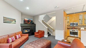 A living room with a fireplace, a sofa, an ottoman, and a kitchen area with wooden cabinets and appliances. - Pacific Place: Mountains On Main (Telluride)