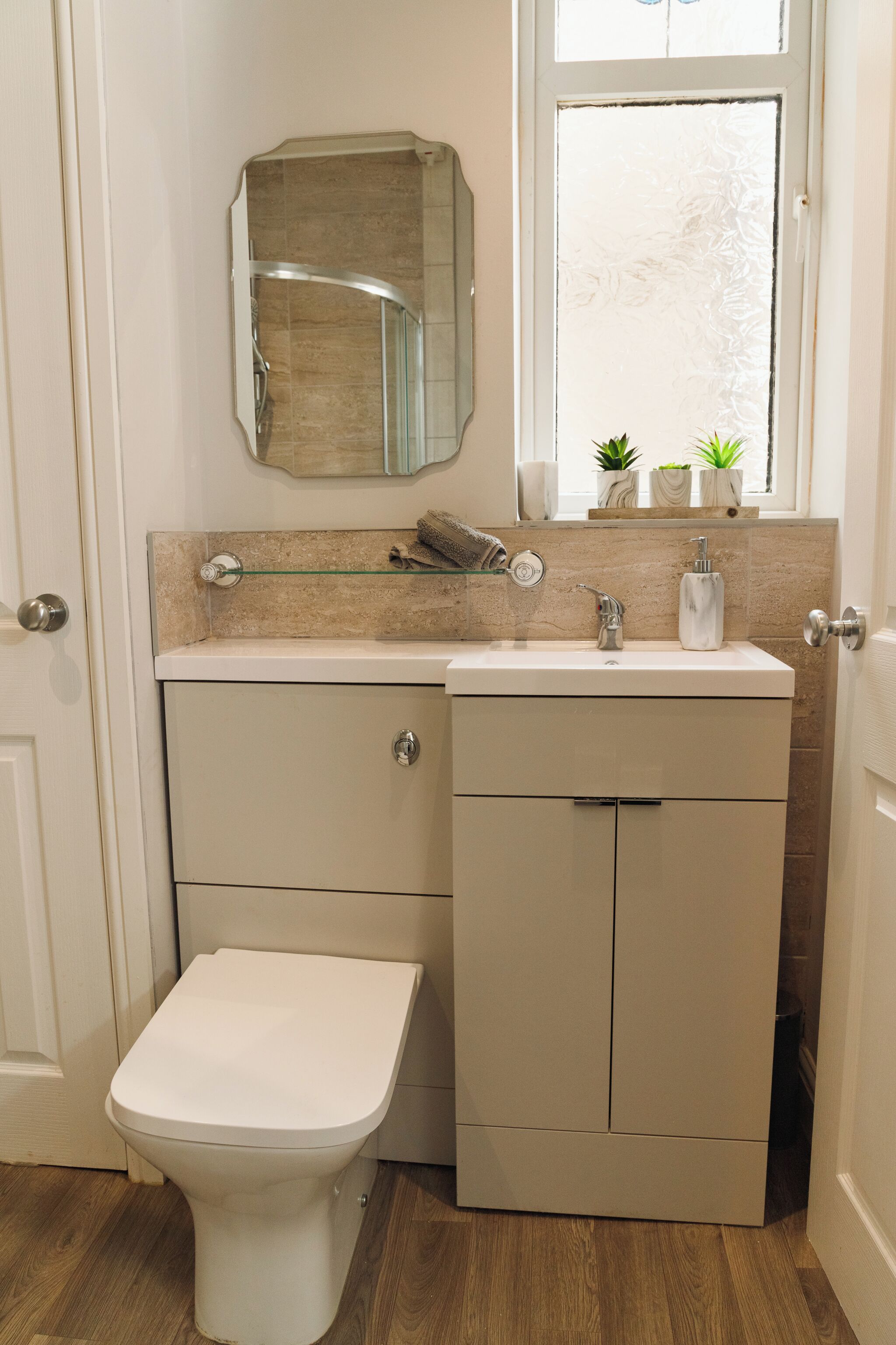 Une salle de bain comprenant des toilettes, un lavabo avec un miroir au-dessus, et une fenêtre avec des plantes sur le rebord.