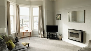 Una sala de estar con sofá, televisión, chimenea y ventanas amplias.