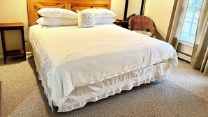 A neatly made bed with white linens, a wooden headboard, and a small bedside table. - The Bond Inn Room #3 (Warrensburg)