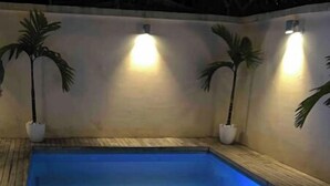 En swimmingpool med blått ljus, omgiven av väggar med planterade växter och väggmonterade lampor.