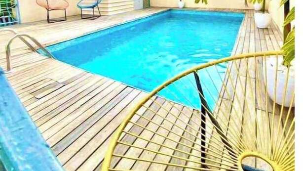 En swimmingpool med ett trädäck, omgiven av planterade växter och två stolar.