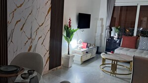 Una sala de estar moderna con una pared con diseño de mármol, un televisor de pantalla plana montado en la pared, un sofá con cojines estampados y una zona de comedor con mesa y sillas.