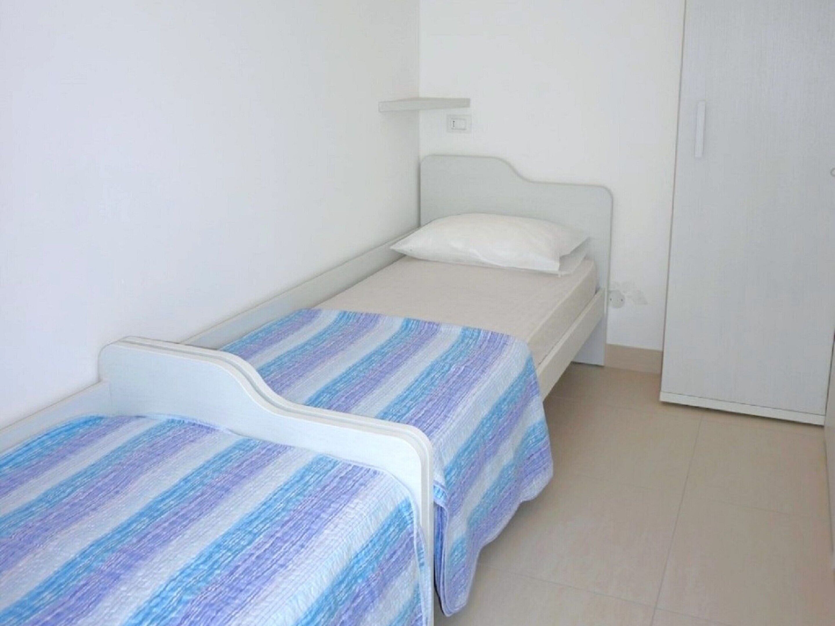 Un petit logement composé d’une seule pièce, comprenant deux lits simples, une armoire blanche et un mur blanc uni.