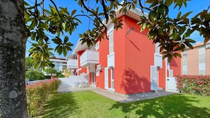 A red building with white shutters, a small patio with chairs, and a well-maintained lawn. - Apartment in Caorle Near Adriatic Beaches (Caorle)