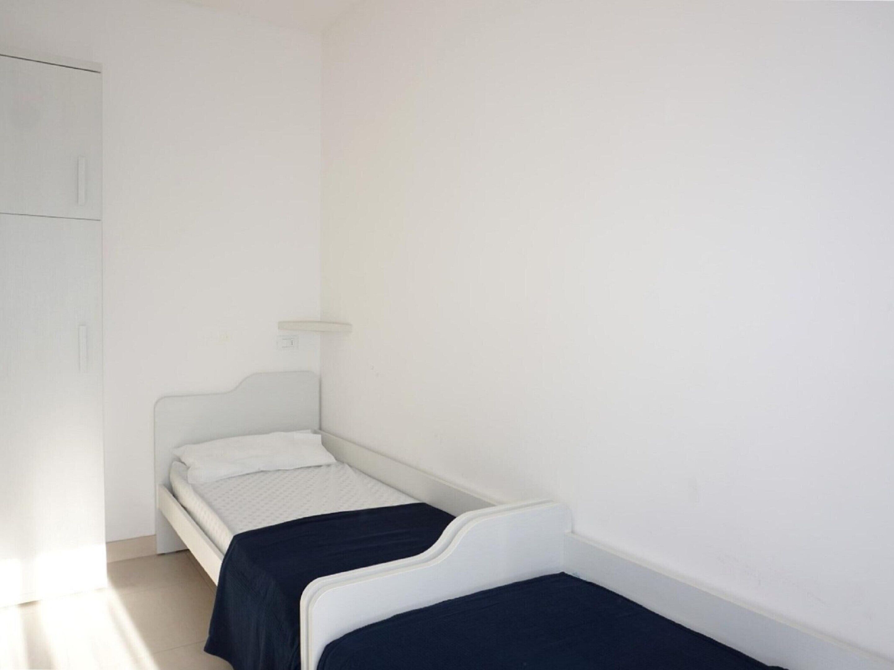 Una habitación pequeña y blanca con dos camas individuales, un armario y un interruptor de luz en la pared.