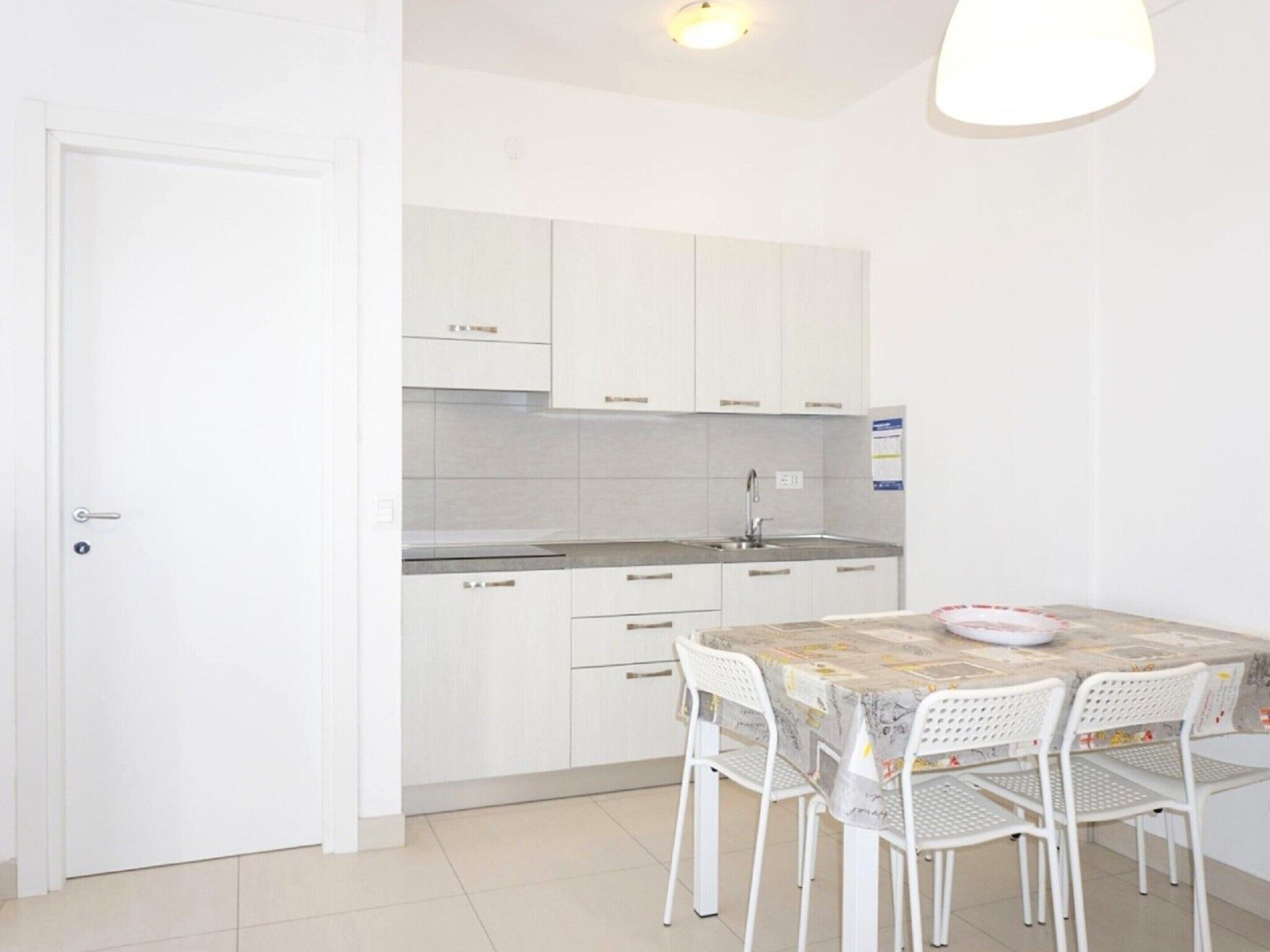 Cocina compacta con gabinetes blancos, un lavamanos y una mesa de comedor con sillas.