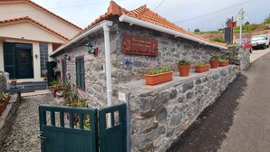 A stone building with a tiled roof, a signboard, and potted plants. - Casa Monte de Paz 1

 (Calheta)
