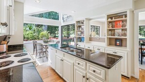 Een moderne keuken met witte kasten, een zwart aanrecht en een groot raam met uitzicht op een tuin.