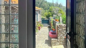 Une porte qui donne sur une cour intérieure, avec un mur en pierre, des plantes en pot et une vue sur une colline.