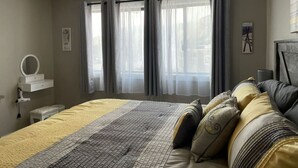 A bedroom with a bed, a ceiling fan, a bedside table with a mirror, and a window with curtains.