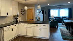 A modern kitchen with white cabinets, a black countertop, and pendant lighting.