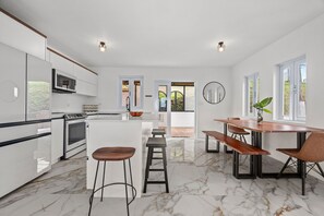 A modern kitchen with white cabinetry, a central island, and a dining area with wooden tables and chairs.