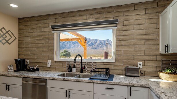 Eine Küche mit großem Fenster, Holzrückwand und Blick auf Berge.