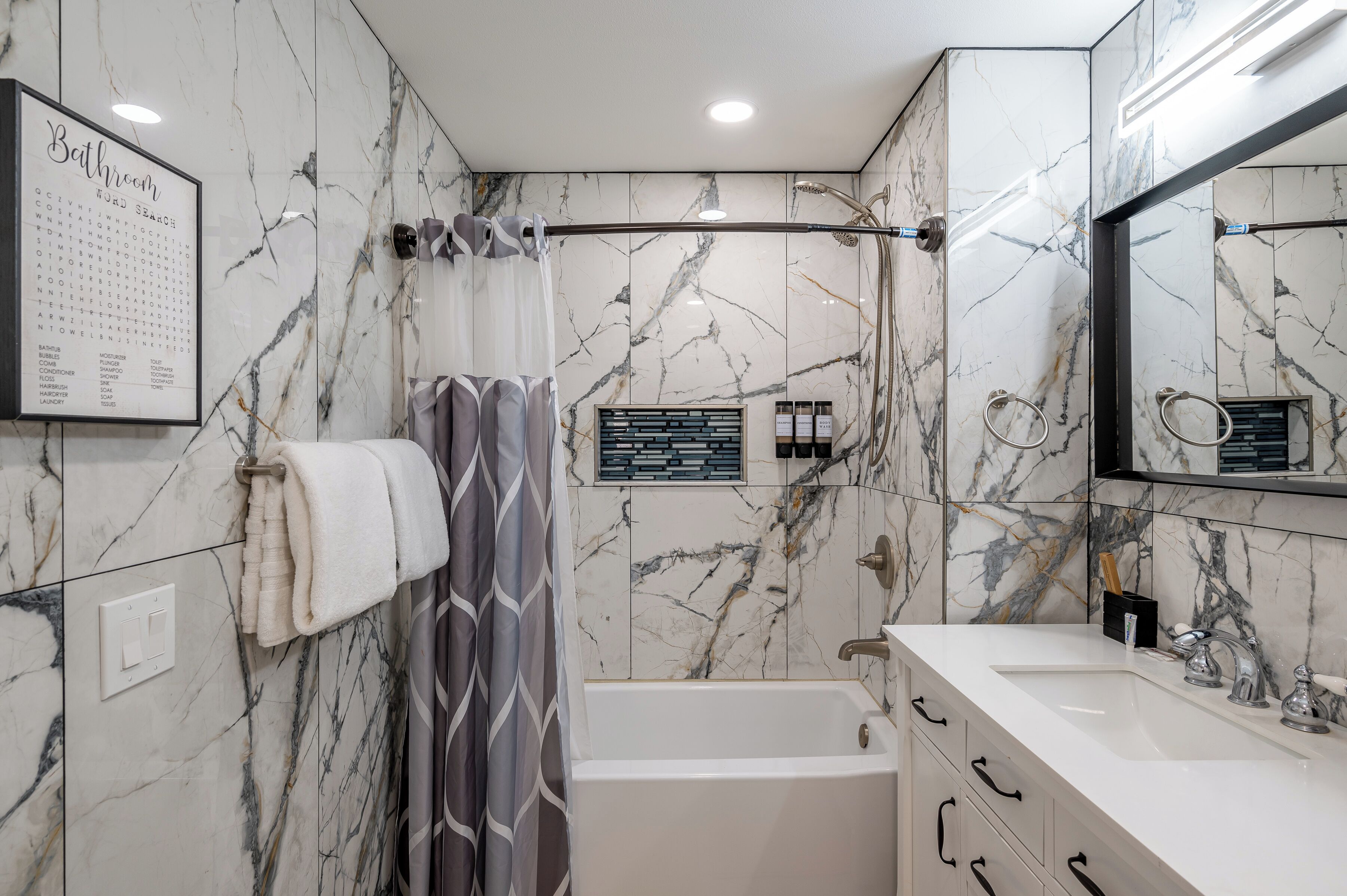 Une salle de bain avec un mur en marbre, une baignoire, un lavabo et un miroir.