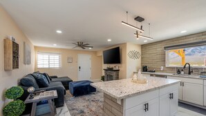 Eine moderne Küche mit einer großen Kochinsel, ein Essbereich mit einer Couch und ein Wohnzimmer mit Deckenventilator und Fernseher.