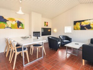 A modern dining area with a white table, wooden chairs, and black leather sofas. There are abstract paintings on the walls and a flat-screen TV mounted above the table. - 6 Person Holiday Park Home in Middelfart (Middelfart)