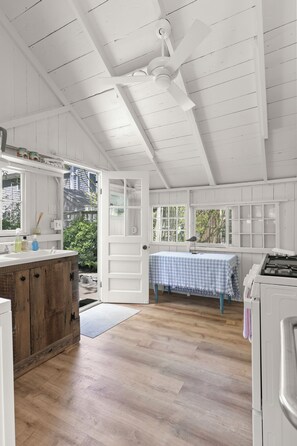 A kitchen with wooden cabinets, a white ceiling fan, and a window with a view of greenery.