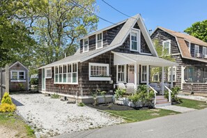 A two-story house with a sloped roof, a covered porch, and a small front yard with plants.