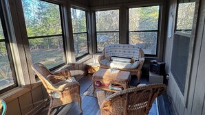 A sunroom with wicker furniture, large windows, and a ceiling fan.