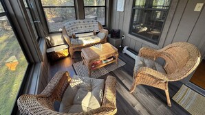 A sunlit room with wicker furniture, large windows, and a view of the outdoors.