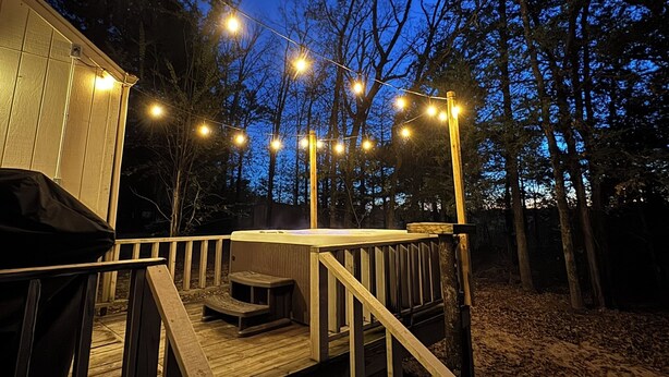 A wooden deck with a hot tub, string lights, and a covered seating area.