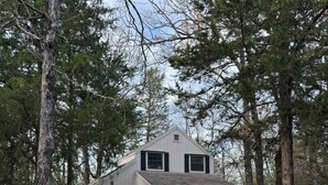 A two-story house with a porch, surrounded by tall trees.